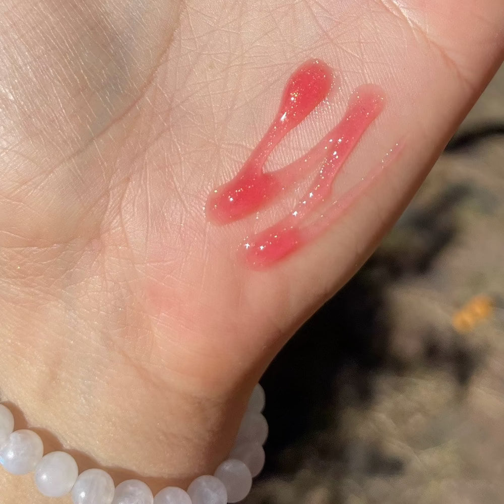 coral lip gloss with gold flecks swatched on palm